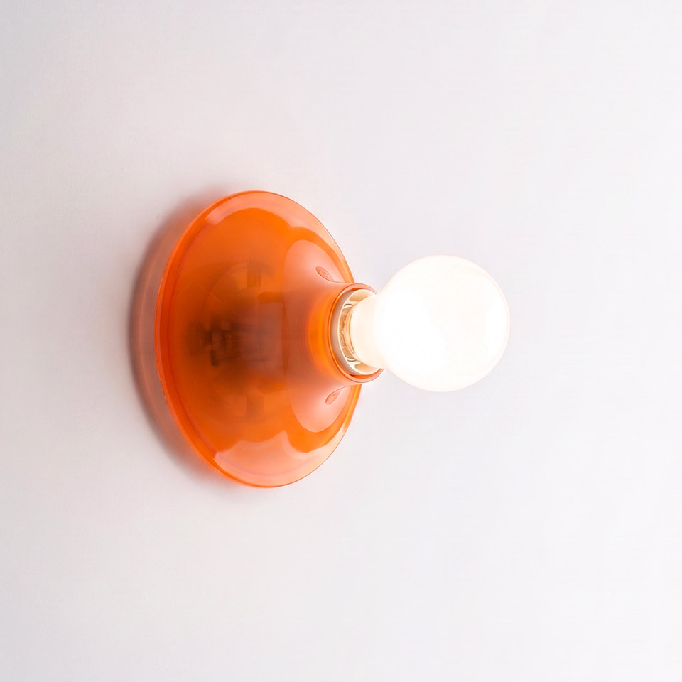 Teti wall lamp by Artemide: translucent orange glass disc base mounted on white wall with exposed Edison-style bulb