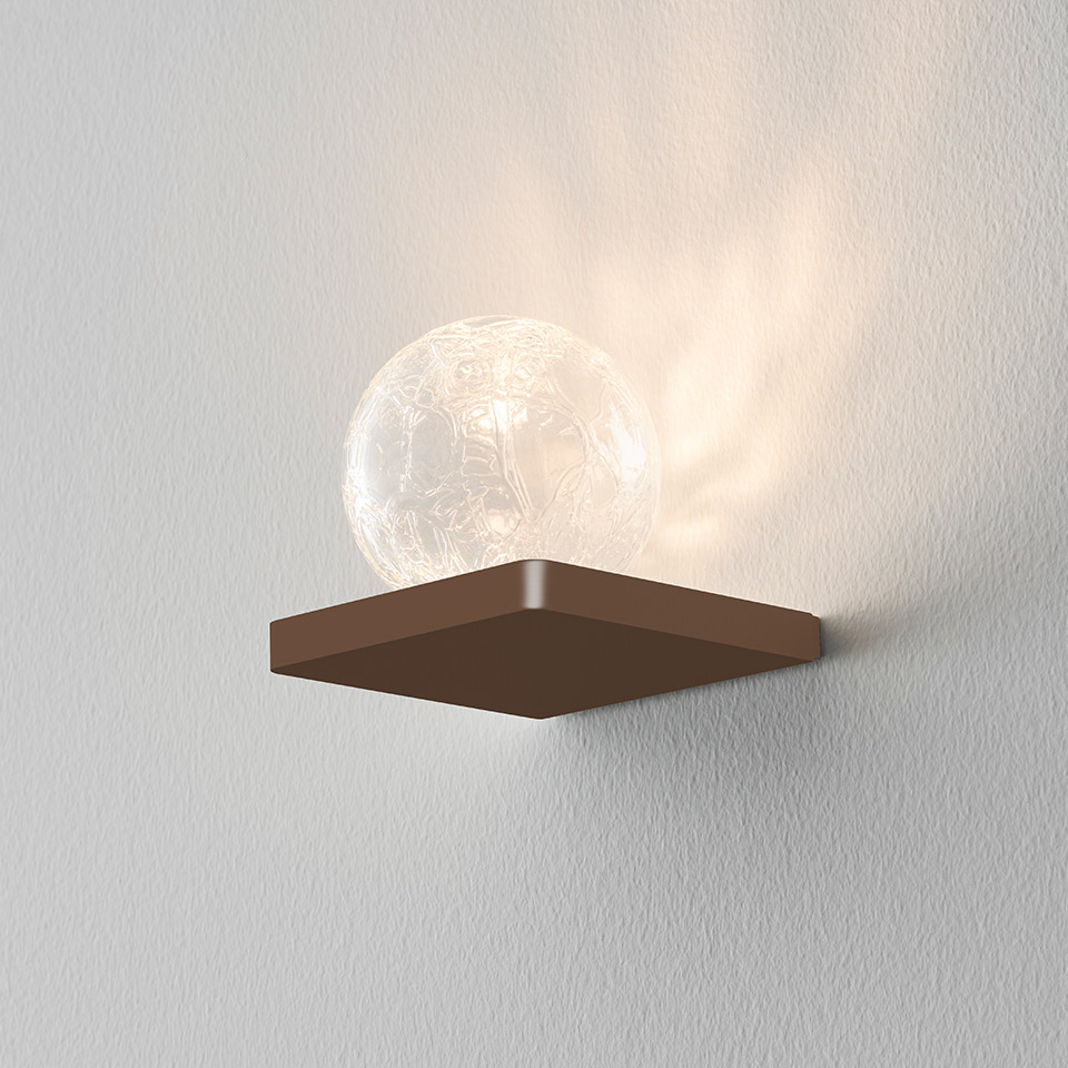 Applique Artemide Ulrich und Diotima: base quadrata bronzo con sfera in vetro craquelé che emette luce calda su parete bianca