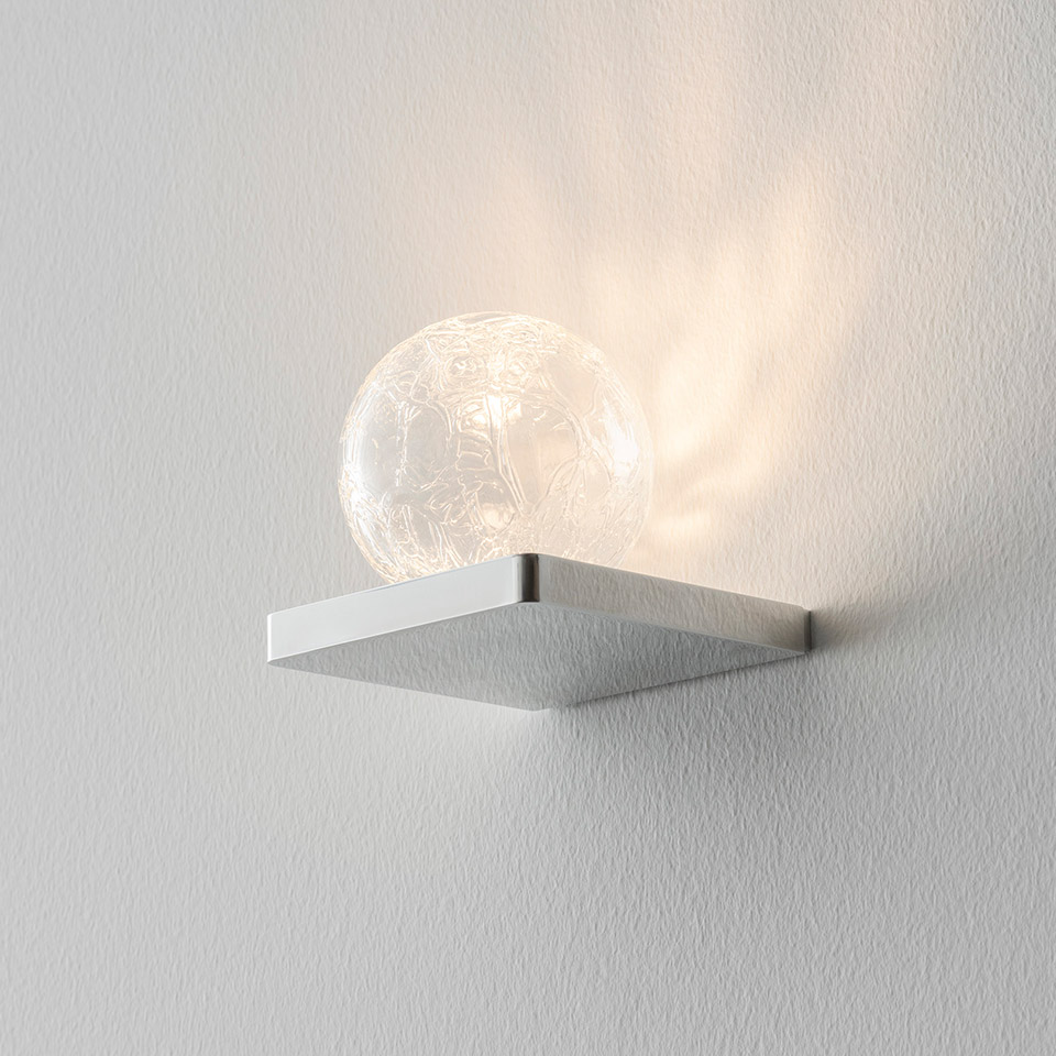 Lampada da parete Artemide Ulrich und Diotima: base quadrata in alluminio spazzolato con sfera in vetro cristallo che proietta motivi luminosi decorativi sulla parete