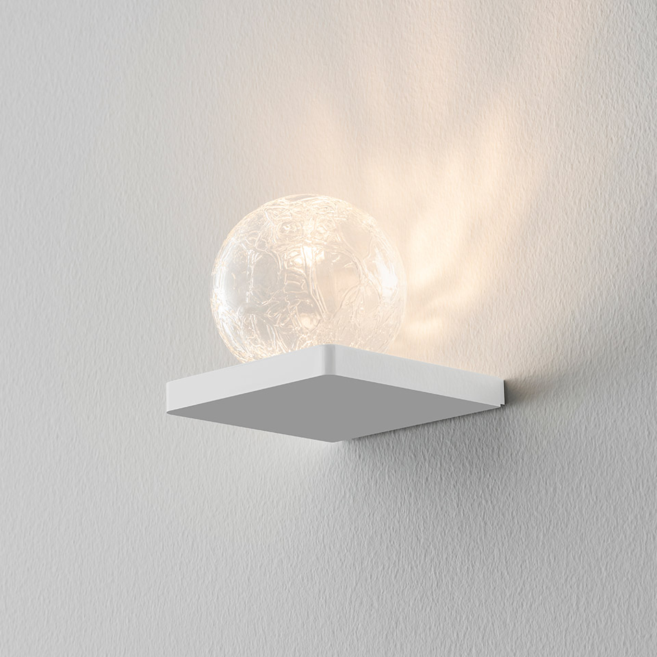 Applique Artemide Ulrich und Diotima: base quadrata bianca con sfera in vetro cristallo strutturato che emette caldi motivi luminosi decorativi