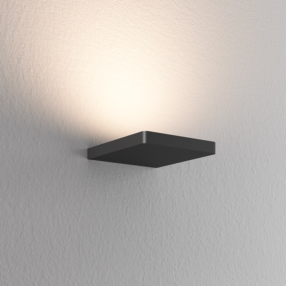 Lampada da parete Artemide Ulrich und Diotima, corpo quadrato in metallo scuro a parete, emette luce indiretta calda verso l'alto