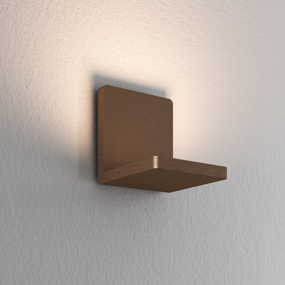 Lampada da parete Artemide Ulrich und Diotima in finitura bronzo spazzolato, corpo quadrato che proietta luce indiretta calda verso l'alto su parete bianca