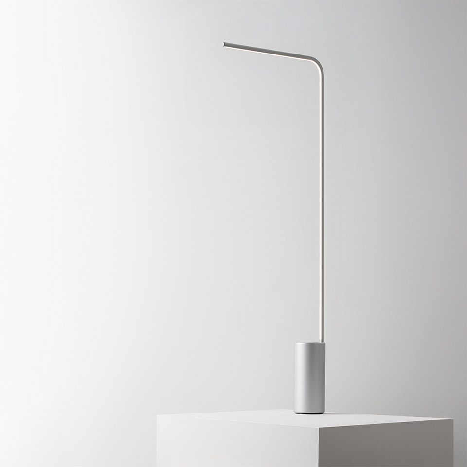 Artemide Veil table lamp: slender white stem with gentle curve, integrated LED light bar, cylindrical base on white surface