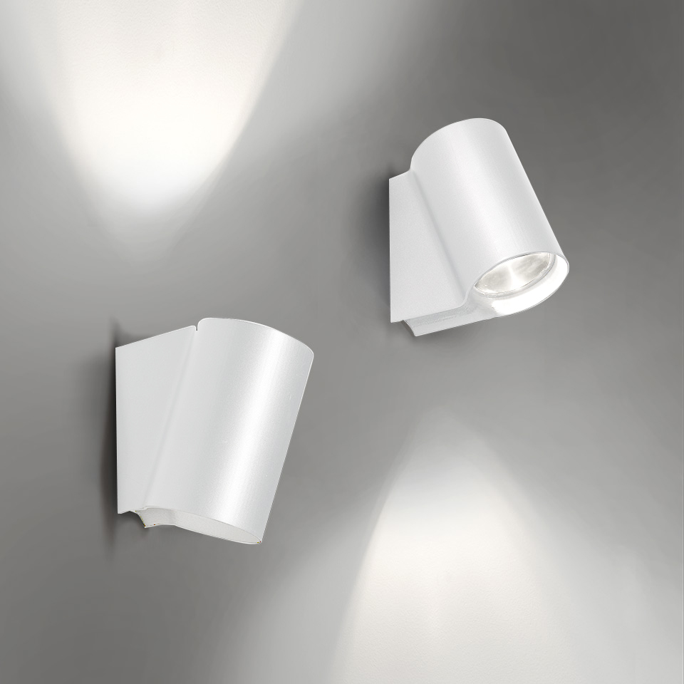 Due faretti da parete Artemide Oblique bianchi: sinistra inclinato verso l'alto con luce sulla parete, destra orientato verso il basso con sorgente LED visibile