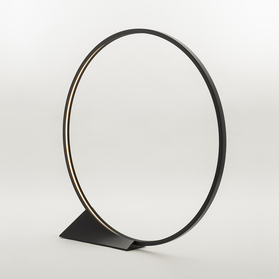 Lampada da tavolo Artemide O: anello circolare LED nero minimalista su base triangolare piatta, con luce calda sul bordo interno