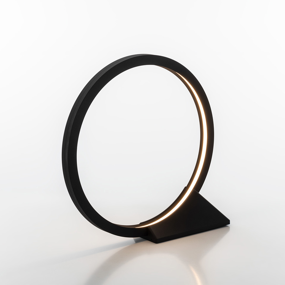 Lampada da tavolo Artemide O: anello circolare nero opaco con striscia LED integrata a luce calda, montata su base triangolare