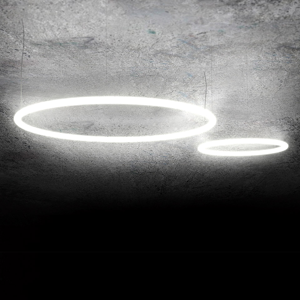 Due sospensioni circolari LED Artemide Alphabet of Light montate inclinate su soffitto in cemento, una grande e una piccola
