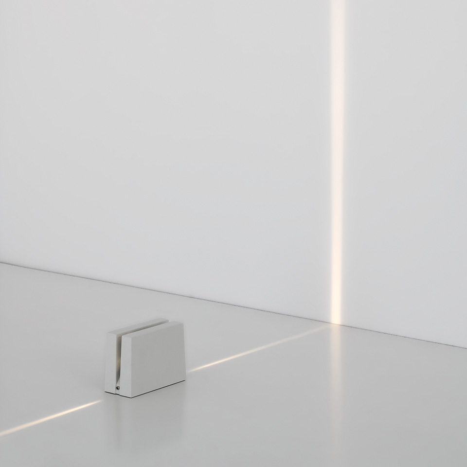 Lampada da terra Antarktikós di Artemide: cubo bianco compatto che emette un fascio di luce verticale preciso lungo l'angolo di una parete bianca