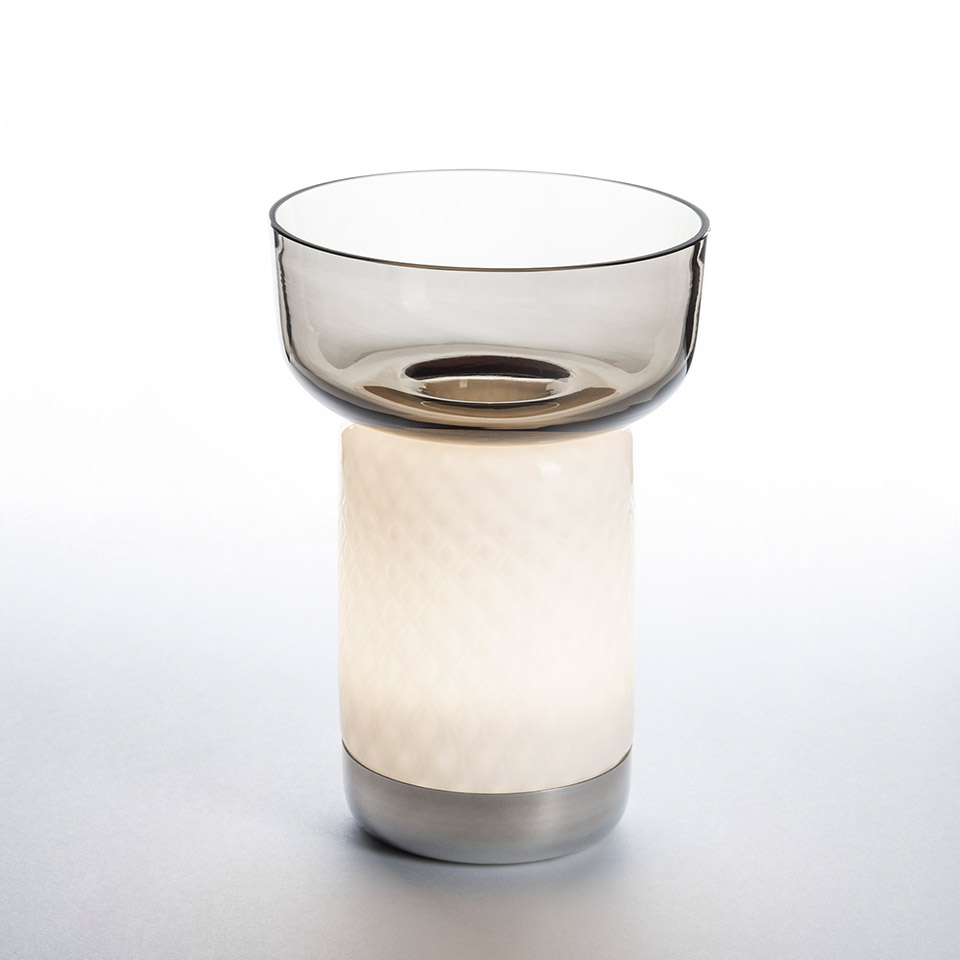 Artemide Bontà table lamp: glowing white textured cylindrical base with smoked glass bowl on top, metal base ring