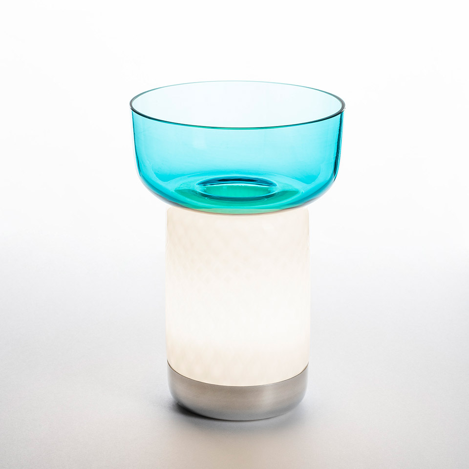 Artemide Bontà table lamp: glowing white cylindrical base with brushed metal bottom and translucent turquoise glass bowl on top