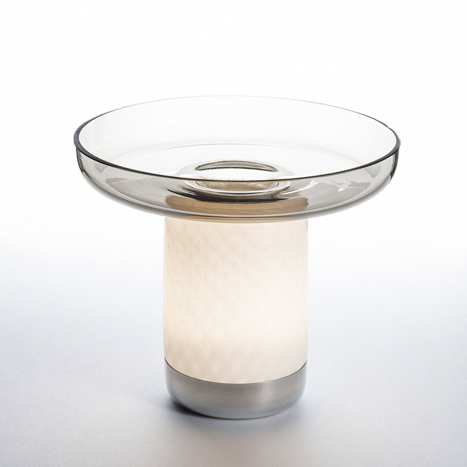 Artemide Bontà table lamp: glowing white cylindrical base with textured glass, topped by a wide transparent smoke-glass bowl