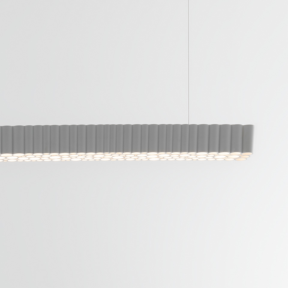 Lampada a sospensione Artemide Calipso Linear System: corpo allungato grigio con diffusori cilindrici ripetuti che emettono luce soffusa verso il basso