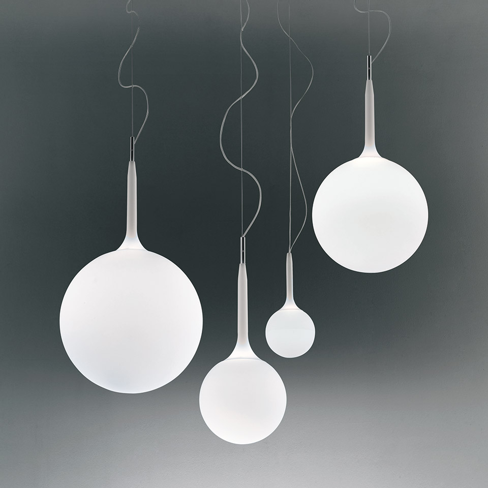 Four Artemide Castore pendant lamps in varying sizes, featuring white opal glass spheres with tapered metal stems on thin cables