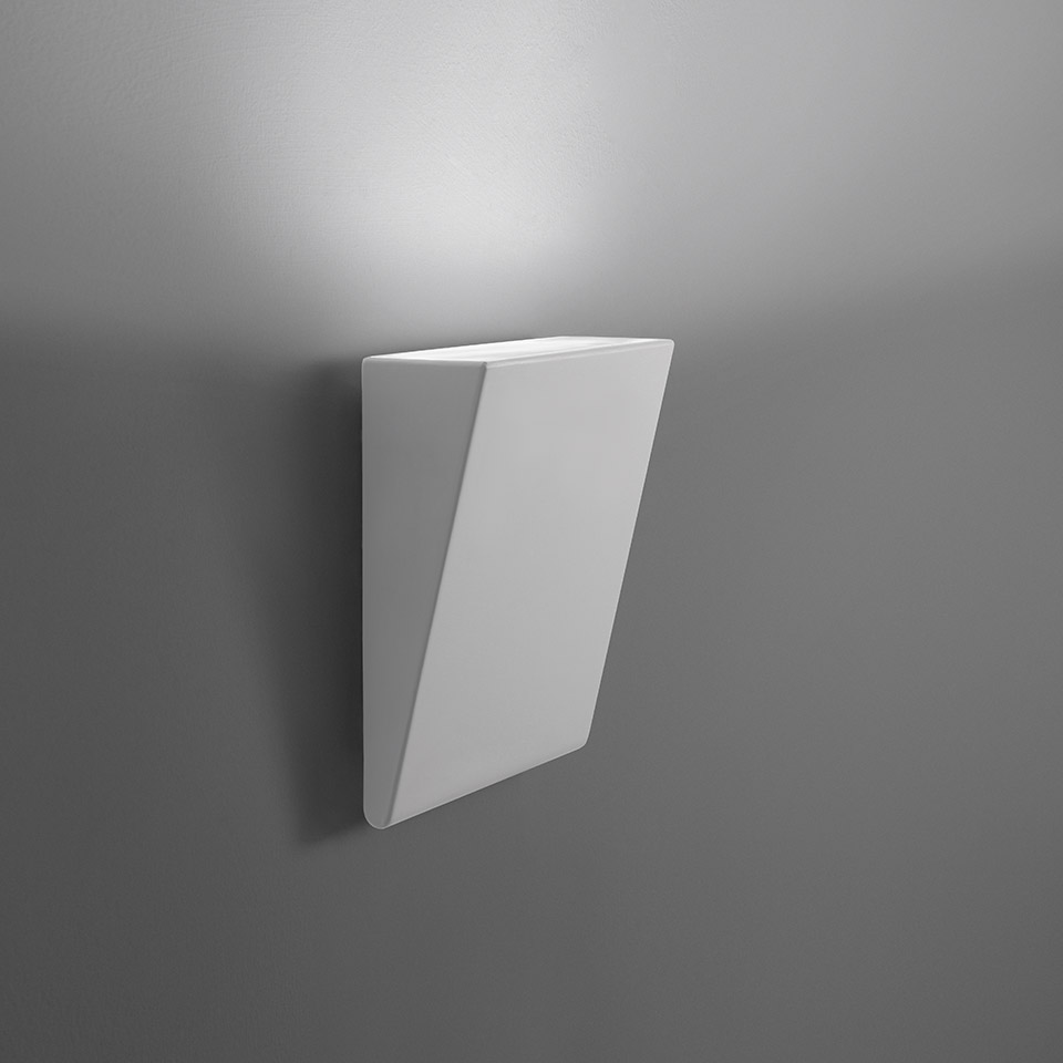 Applique da parete Artemide Cuneo, corpo geometrico angolare bianco che emette luce indiretta verso l'alto su parete grigia