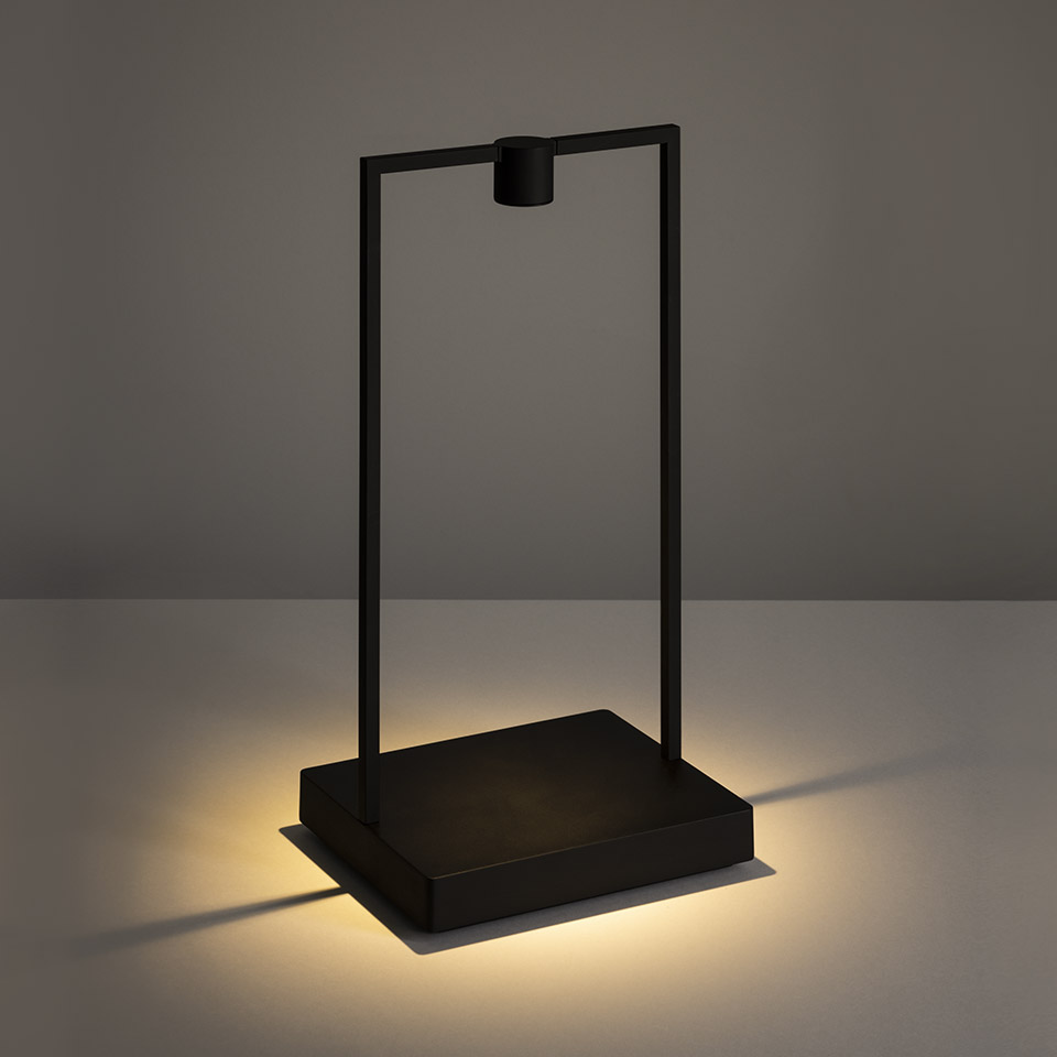 Lampada da tavolo Artemide Curiosity: struttura rettangolare nera minimalista con sorgente LED sospesa, luce calda emanata dalla base quadrata