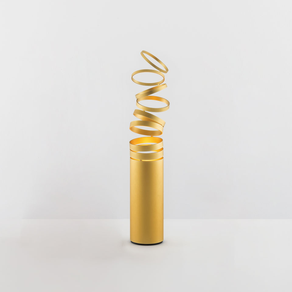 Lampada da tavolo Artemide Decomposé Light Tavolo in oro, con base cilindrica e paralume a nastro spiralato verso l'alto.