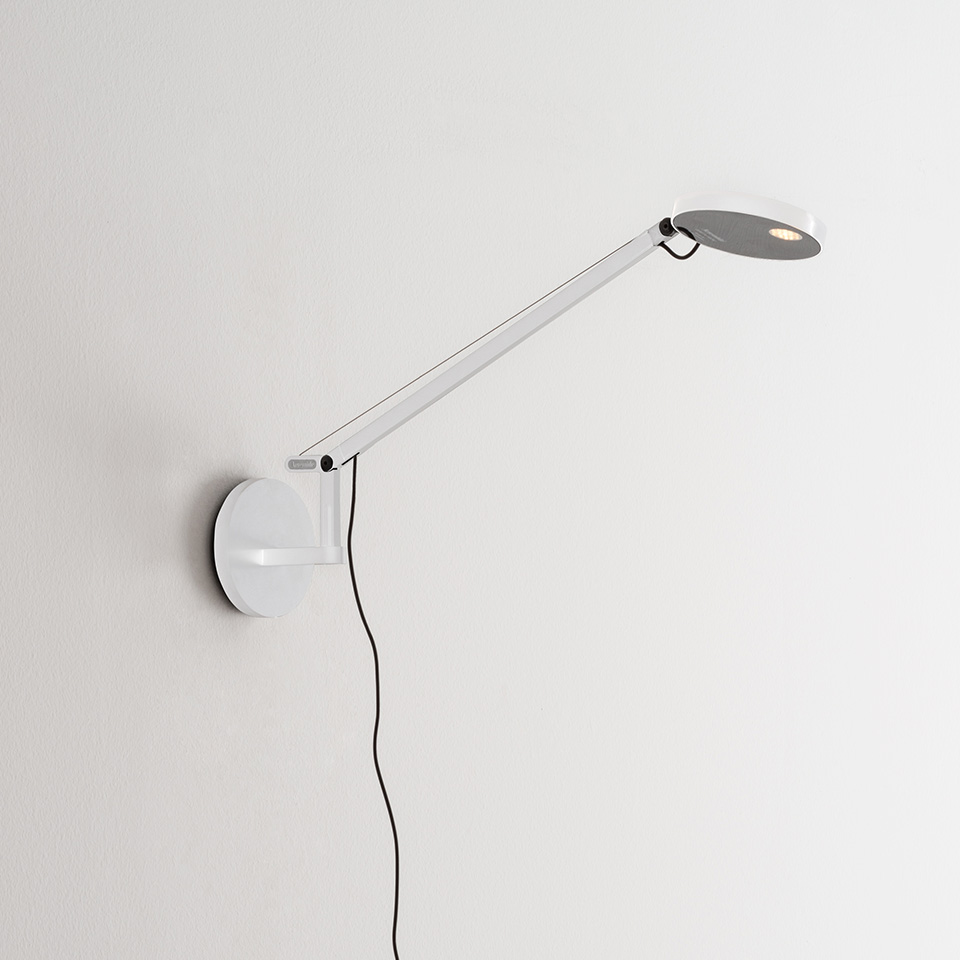 Artemide Demetra Micro Parete wall lamp in white, featuring an adjustable arm and oval LED head, mounted on a round wall base with black cord