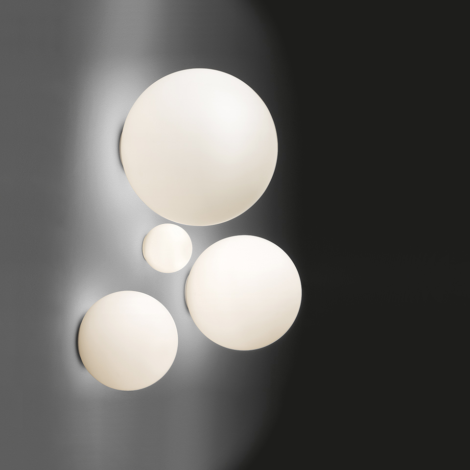 Quattro lampade da parete/soffitto Artemide Dioscuri in diverse dimensioni, sfere in vetro opalino bianco montate su una parete scura creando un effetto costellazione