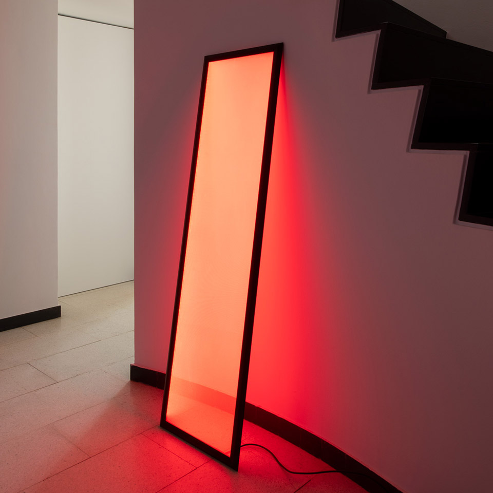 Lampada da terra Artemide Discovery Terra con cornice nera appoggiata alla parete, emette luce rossa vibrante, illumina area scala