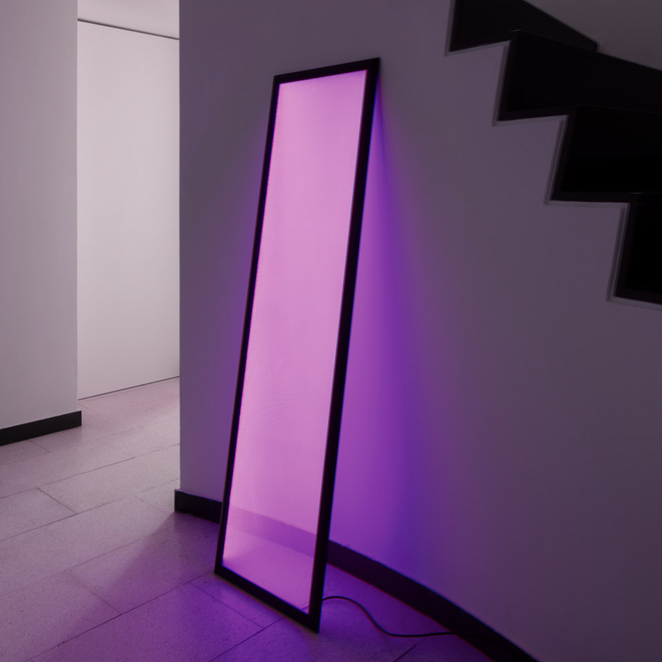 Lampada da terra Artemide Discovery Terra appoggiata alla parete, emette luce viola vibrante, illumina lo spazio vicino alla scala