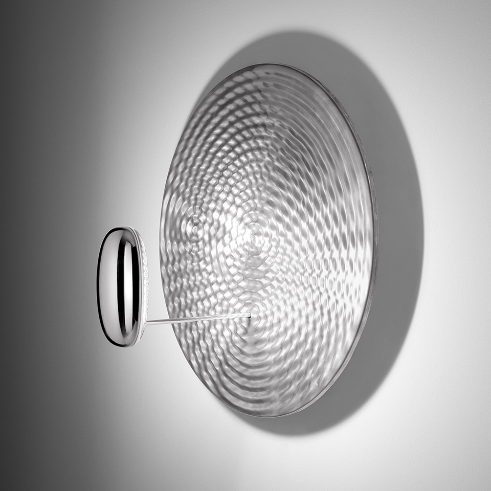 Artemide Droplet wall lamp: circular textured glass diffuser with concentric wave pattern, mounted on chrome wall bracket, casting decorative shadow