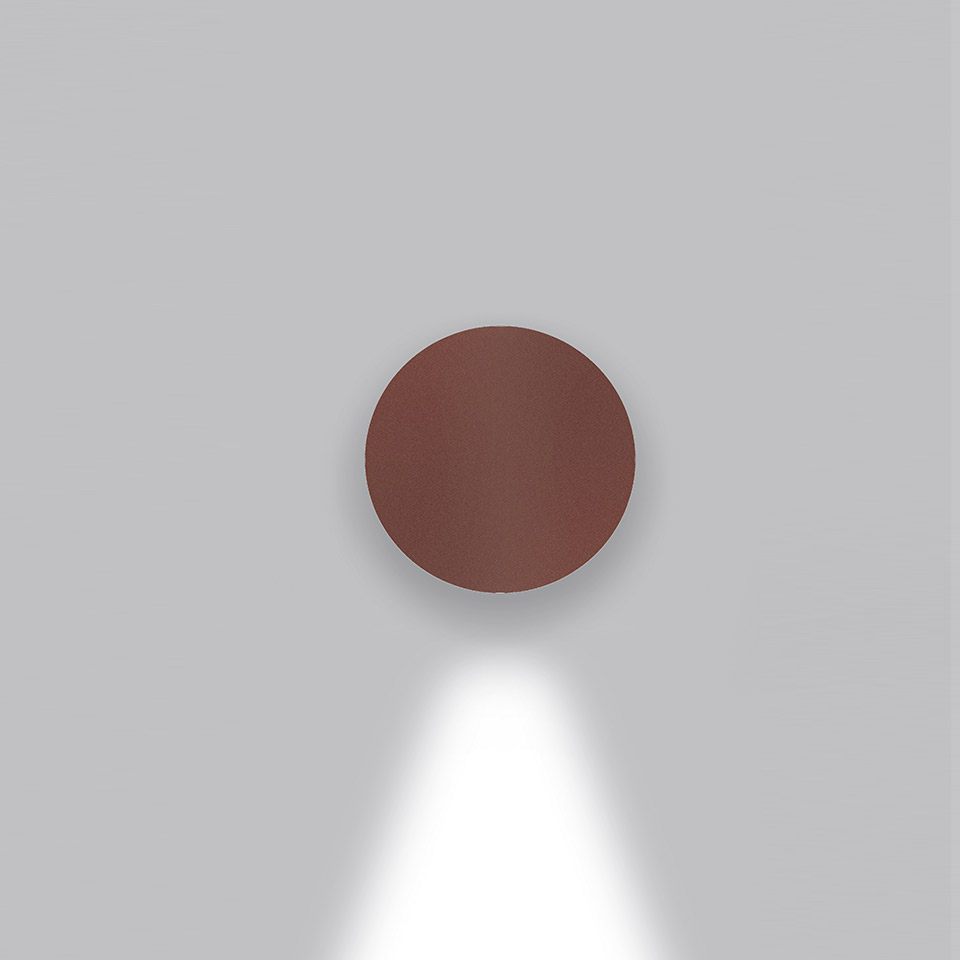 Applique da parete Artemide Effetto color bordeaux, forma circolare a disco, con fascio di luce bianca diretto verso il basso su parete grigia