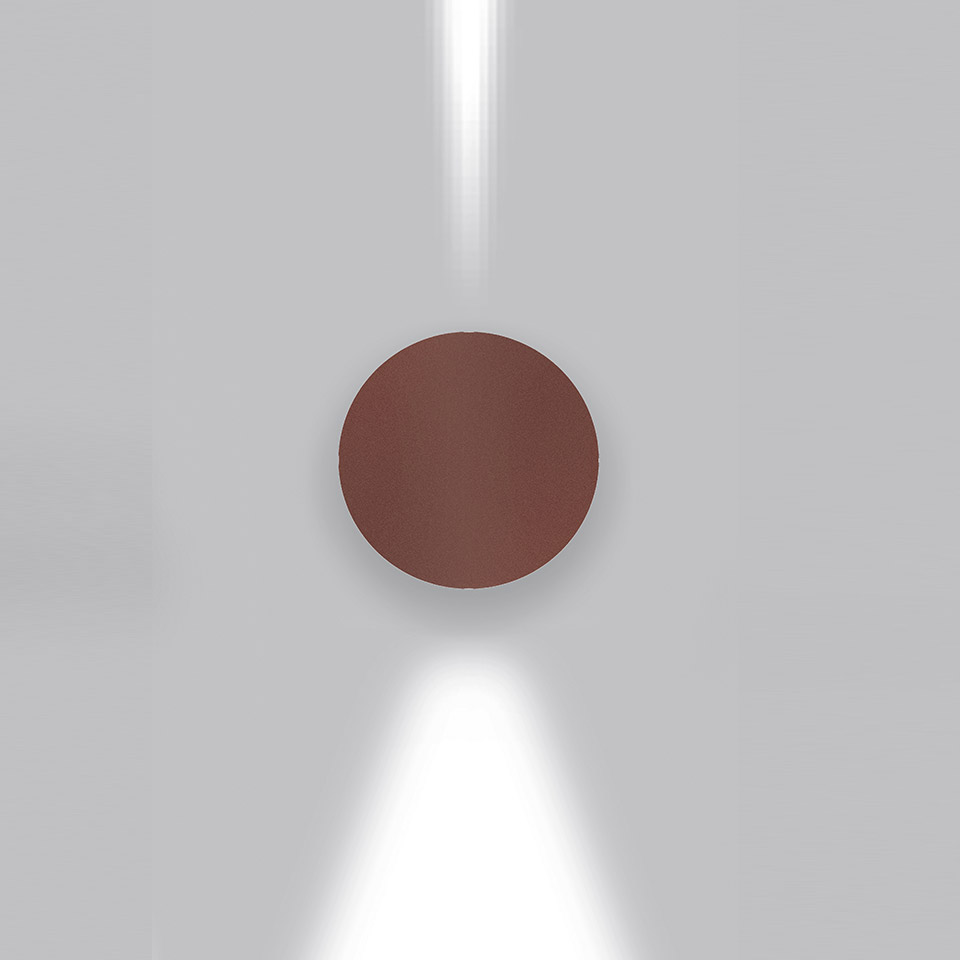 Lampada da parete Artemide Effetto in finitura marrone-rosso, con due fasci di luce stretti diretti verso l'alto e il basso su parete grigia