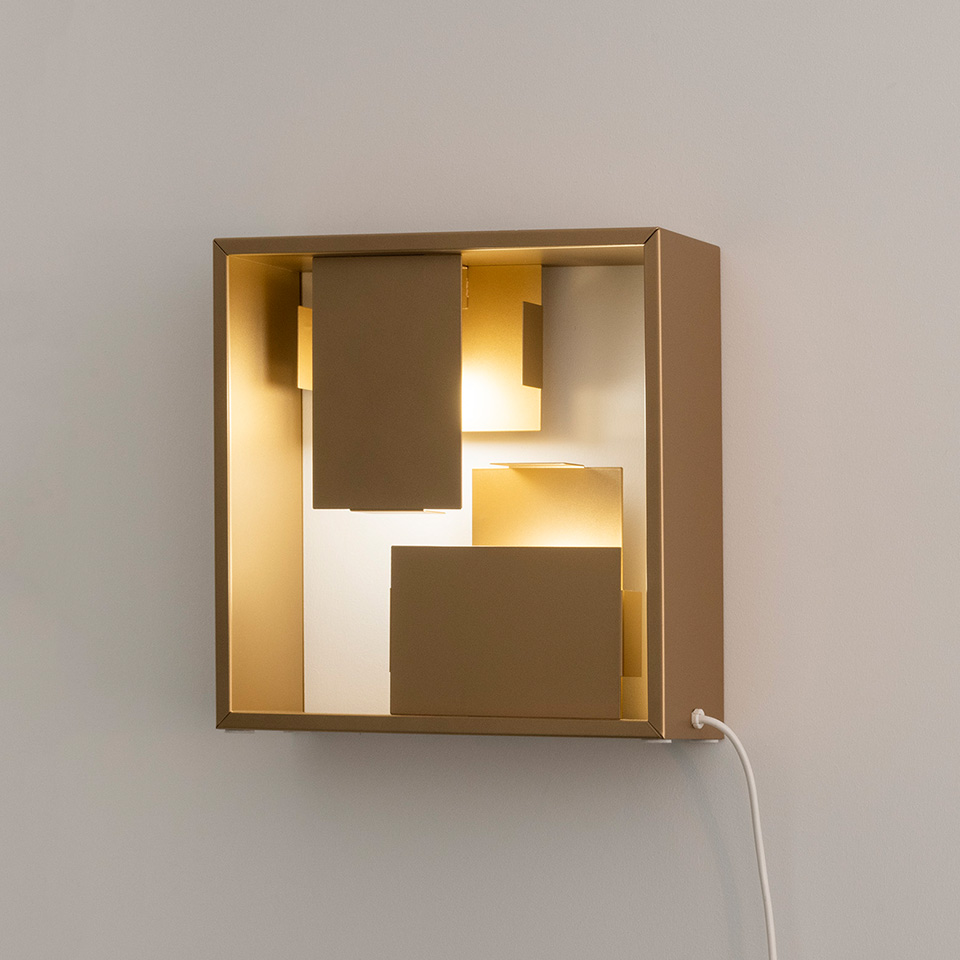 Artemide Fato wall lamp: square gold-toned metal box with layered geometric panels creating warm indirect LED light