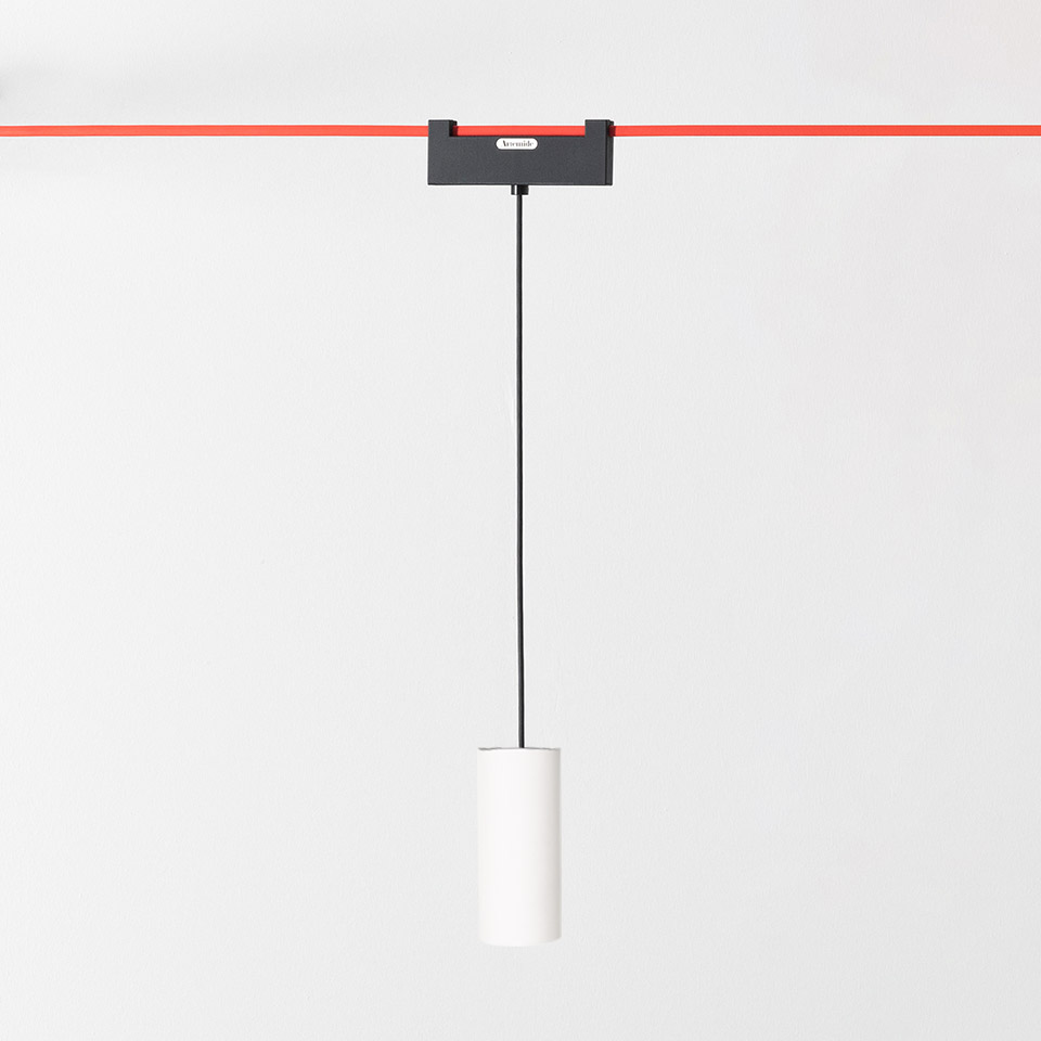 Artemide Funivia pendant lamp: white cylindrical shade hanging from black cord, mounted on dark adapter on red ceiling track