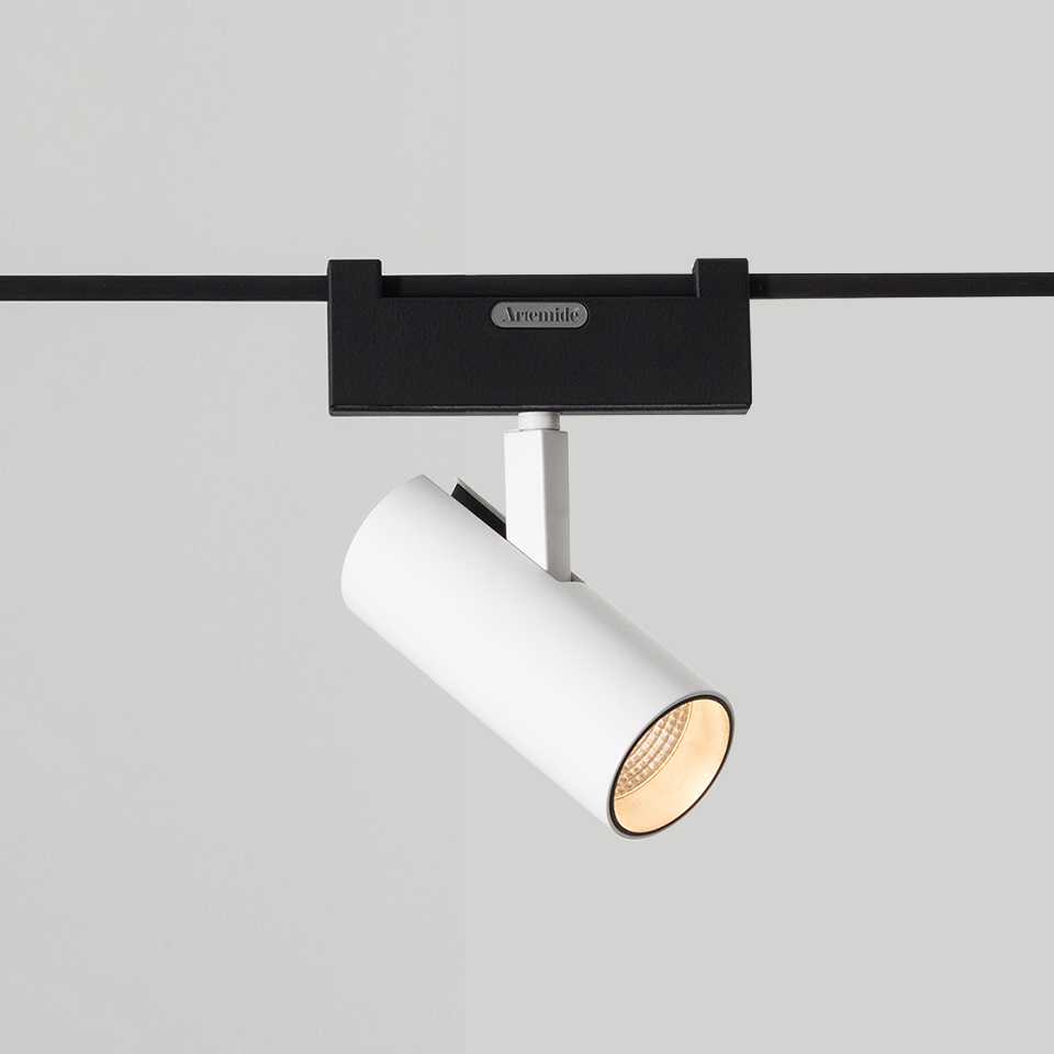 Artemide Funivia track spotlight: white cylindrical LED spot mounted on black track rail, tilted to direct warm light downward
