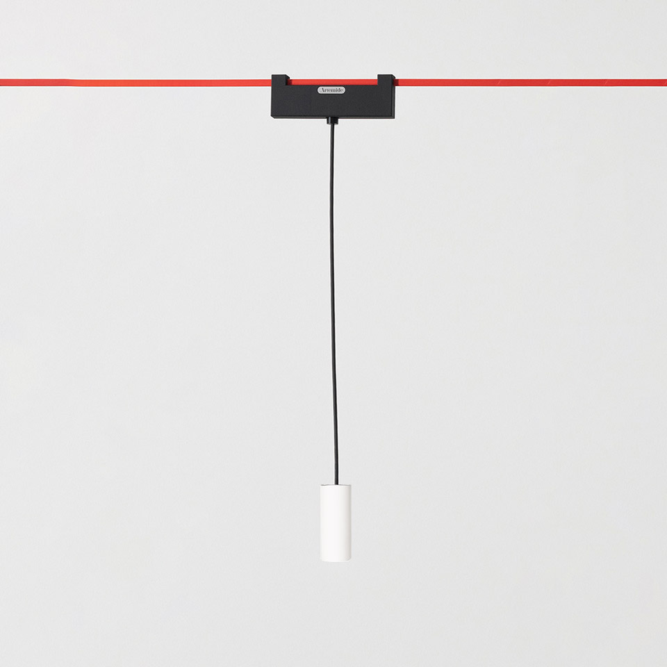 Artemide Funivia pendant lamp: white cylindrical fixture hanging from black cord, mounted on black adapter clipped to red cable system