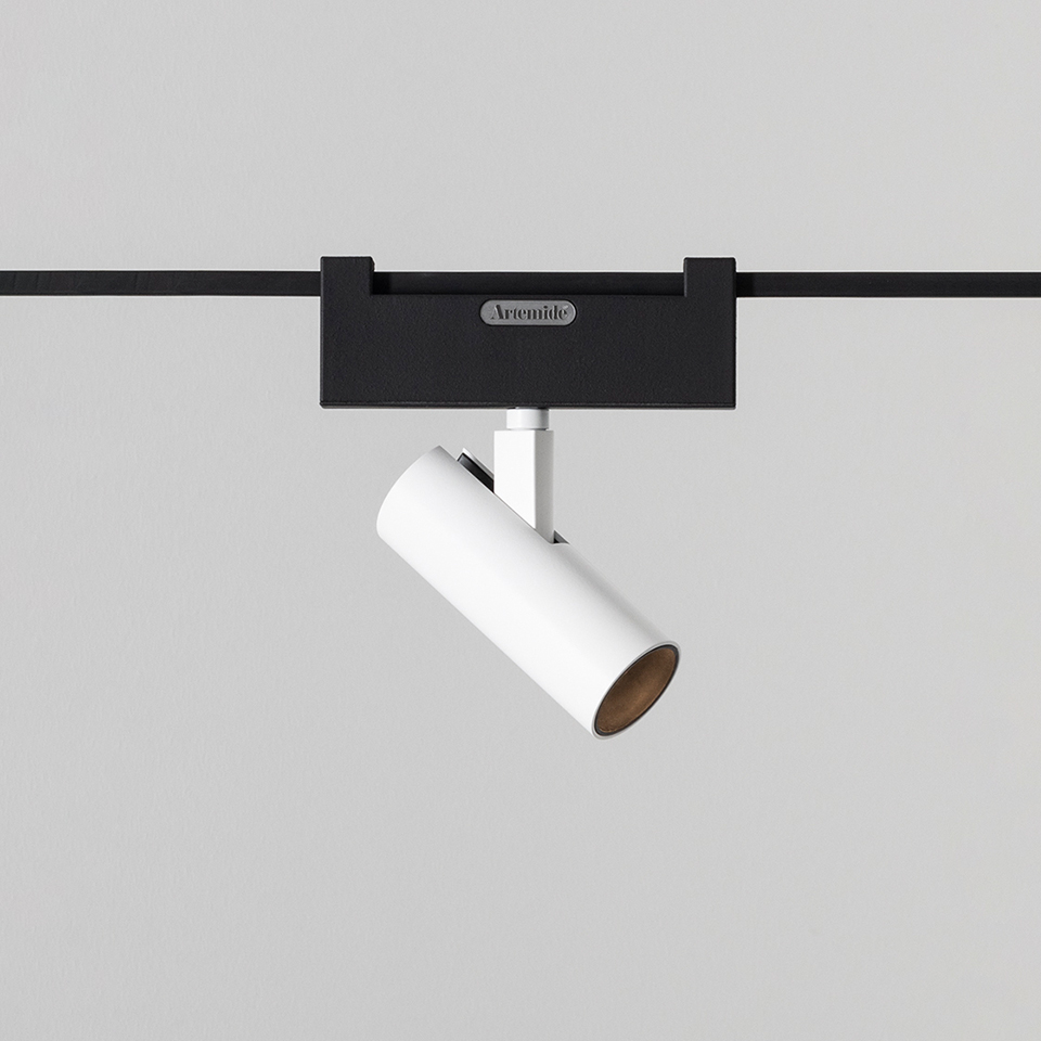 Artemide Funivia track spotlight: white cylindrical head on black rail adapter, adjustable angle, warm wood interior finish