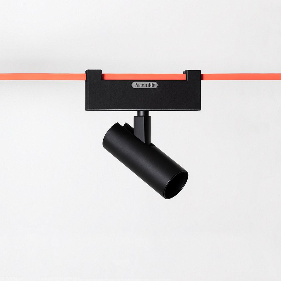 Artemide Funivia black track spotlight with cylindrical head, mounted on a red cable track system against a white background