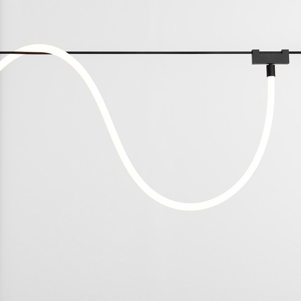 Artemide Funivia: tubo luminoso LED bianco flessibile sospeso a un sistema di binari a cavo nero, che forma un'elegante curva a S