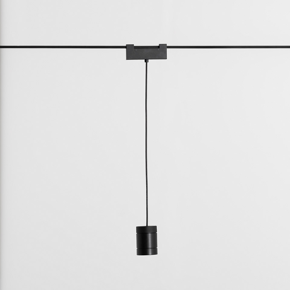 Lampada a sospensione Artemide Funivia nera appesa a binario tramite sottile cavo, con corpo cilindrico compatto nero