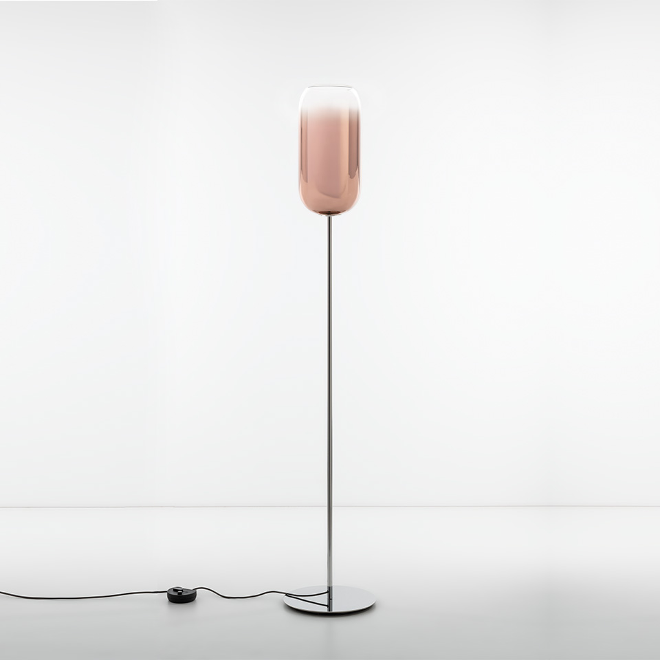 Artemide Gople floor lamp with tall chrome stem, round base, and elongated rose-gold glass diffuser emitting warm ambient light