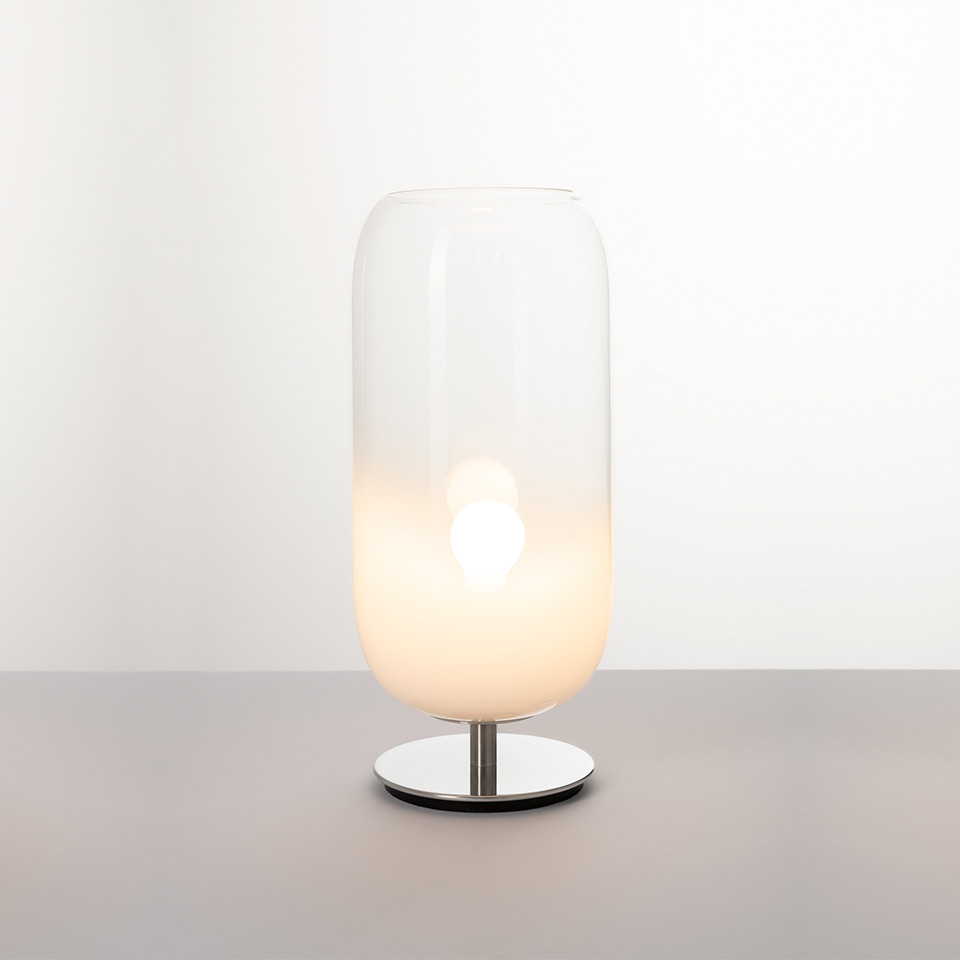 Artemide Gople table lamp: tall cylindrical blown glass shade, white opal gradient, warm glowing light, polished chrome base
