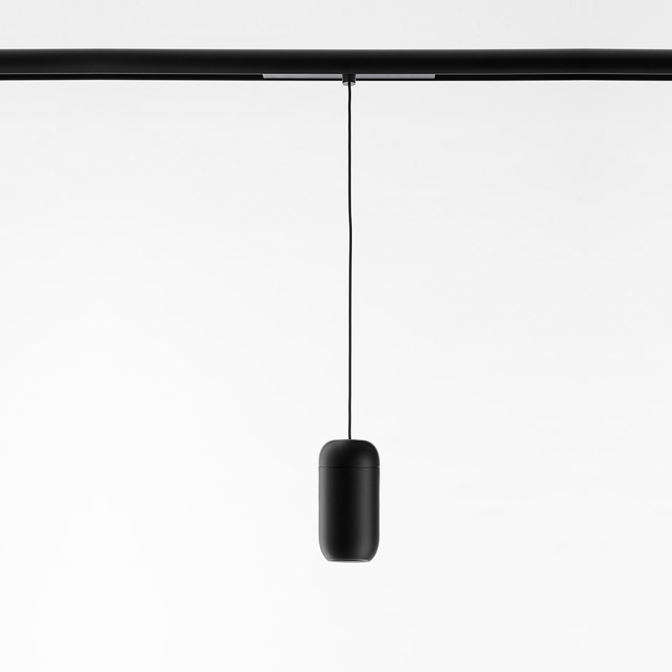 Artemide Gople System: lampada a sospensione nera a forma di capsula appesa con un sottile cavo a un binario nero a soffitto