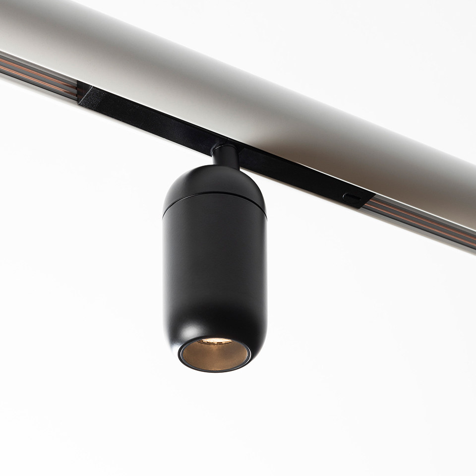 Artemide Gople System: faretti LED cilindrici neri montati su binario a soffitto, con riflettore interno dai toni caldi