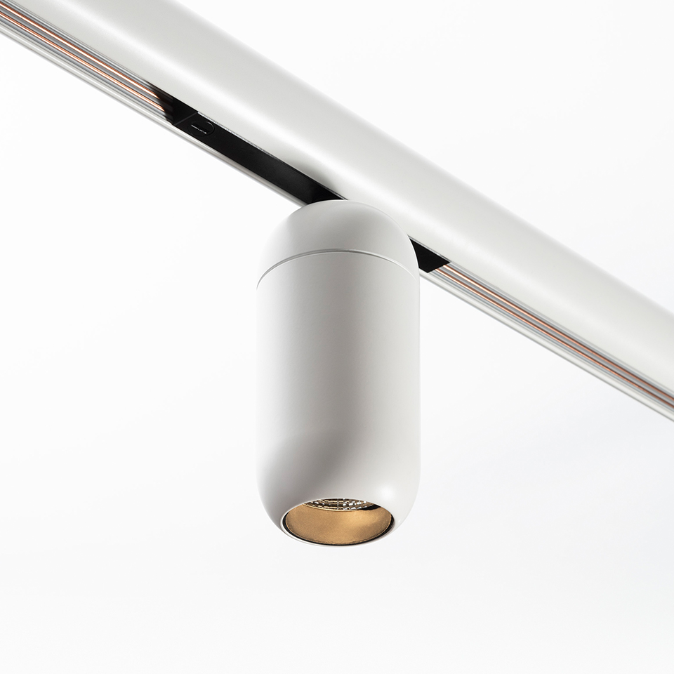 Faretto da binario Artemide Gople System: corpo cilindrico bianco con riflettore interno dorato montato su binario a soffitto bianco