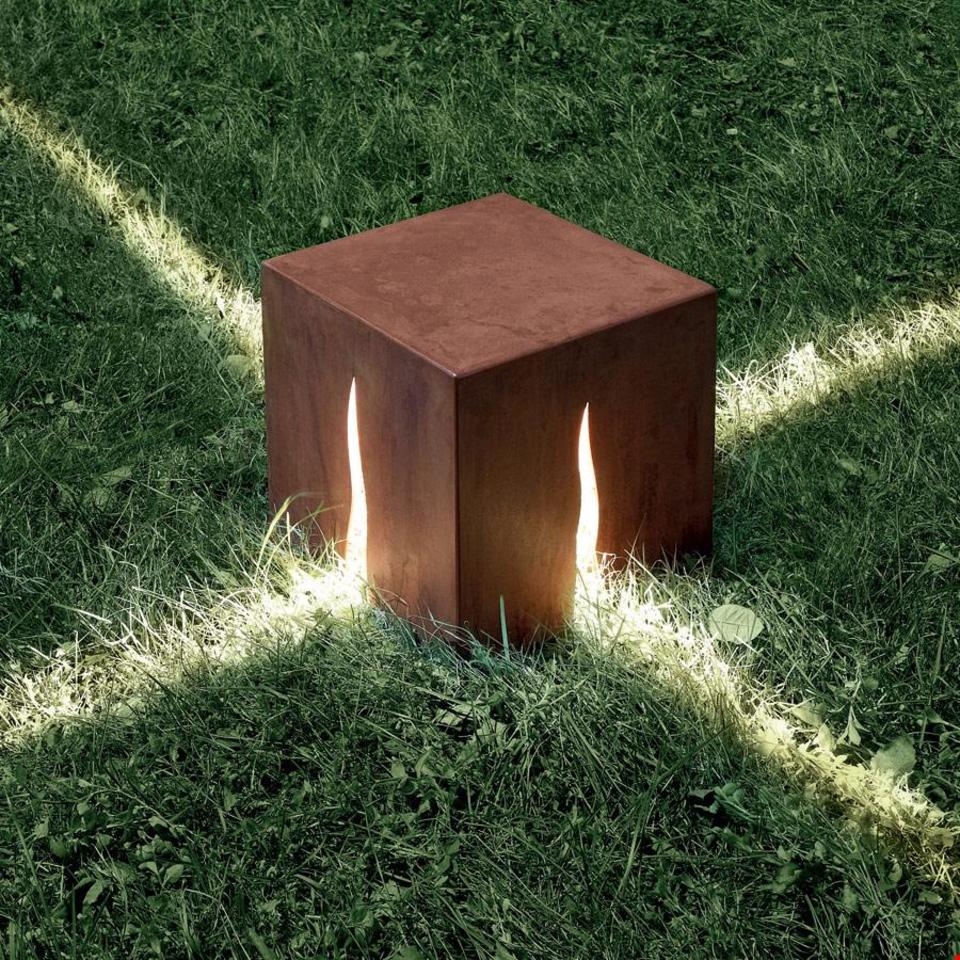 Lampada da terra per esterni Artemide Granito: cubo in acciaio Corten con fessure a fiamma che proiettano raggi di luce sull'erba circostante