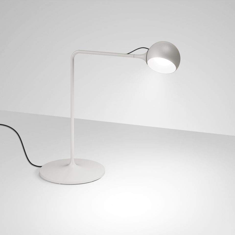 Lampada da tavolo Artemide Ixa bianca con braccio articolato, paralume sferico metallico e base circolare, emette luce calda concentrata