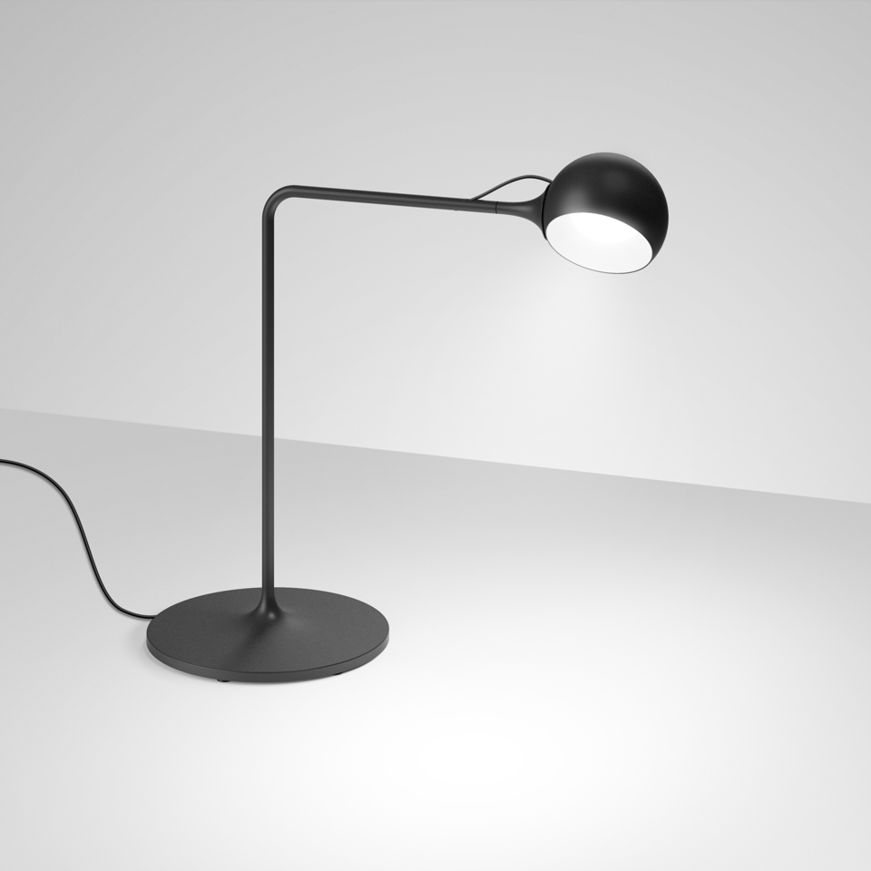 Lampada da tavolo Artemide Ixa nera con base rotonda, braccio curvo e testa sferica orientabile che emette luce bianca concentrata