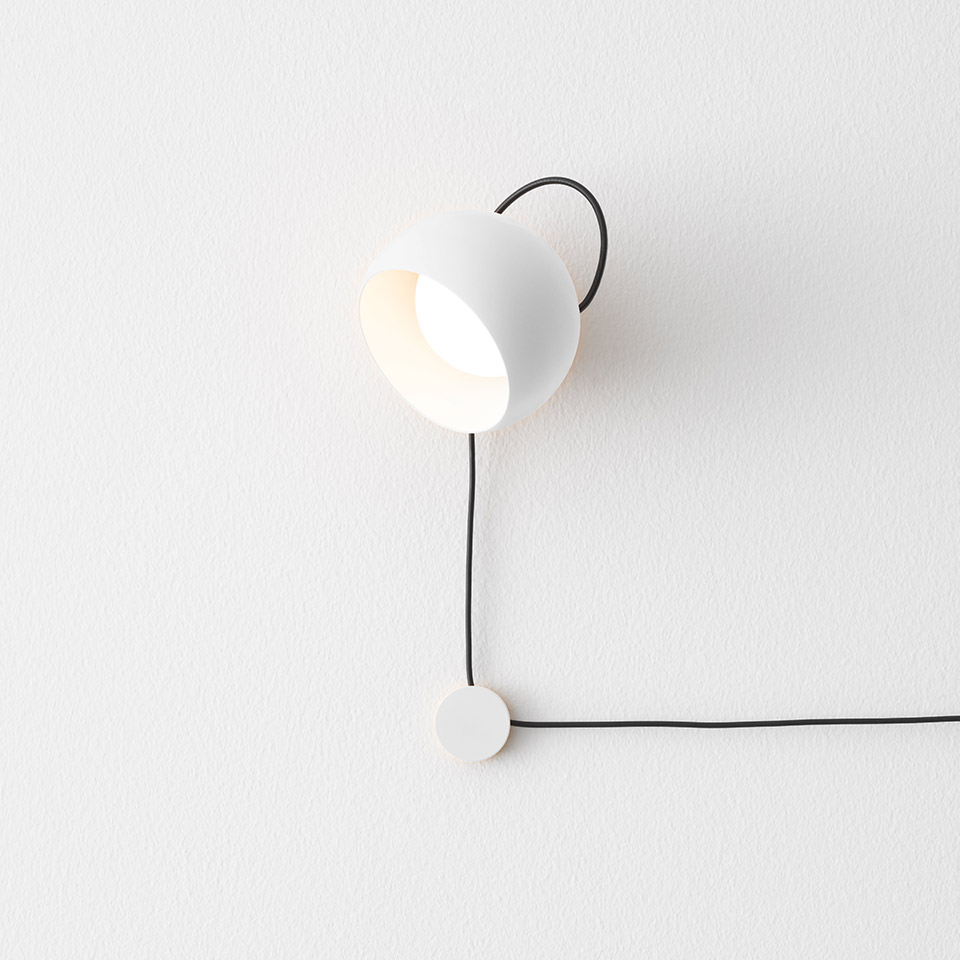 Lampada da parete Artemide Ixa: testa a cupola bianca su braccio curvo nero, orientamento regolabile, con cavo nero e base rotonda
