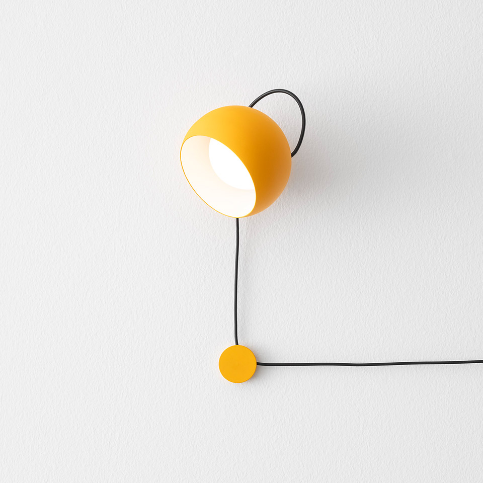 Lampada da parete Artemide Ixa: paralume sferico giallo su arco di filo nero, luce direzionale, con interruttore dimmer circolare giallo in basso