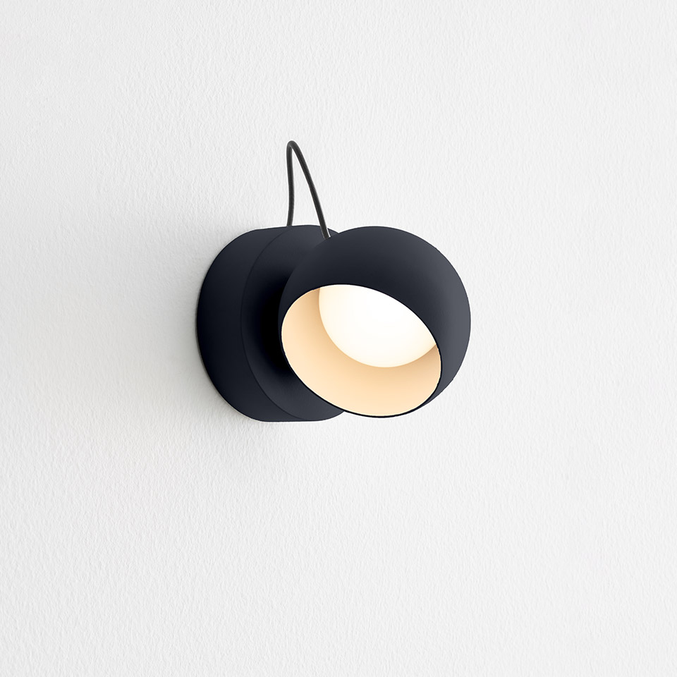 Applique da parete Artemide Ixa nera, con paralume rotondo orientabile e interno bianco caldo, montata su parete bianca