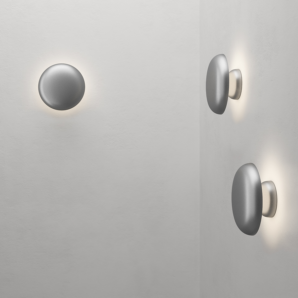 Applique da parete Artemide Knop: elementi rotondi a disco in alluminio montati a parete, con luce indiretta diffusa ad alone intorno ai bordi