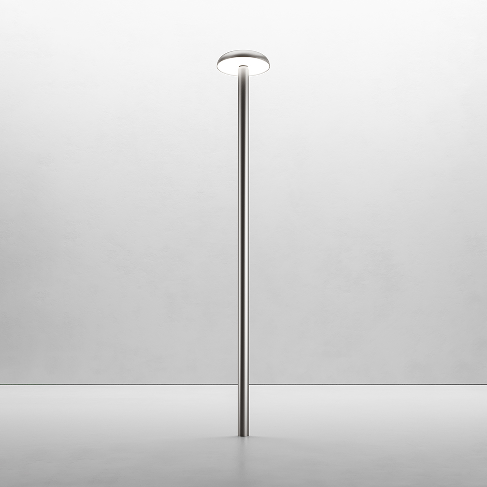 Lampada da terra Artemide Knop: sottile palo in metallo lucido con diffusore LED circolare piatto in cima, che emette luce verso l'alto e il basso