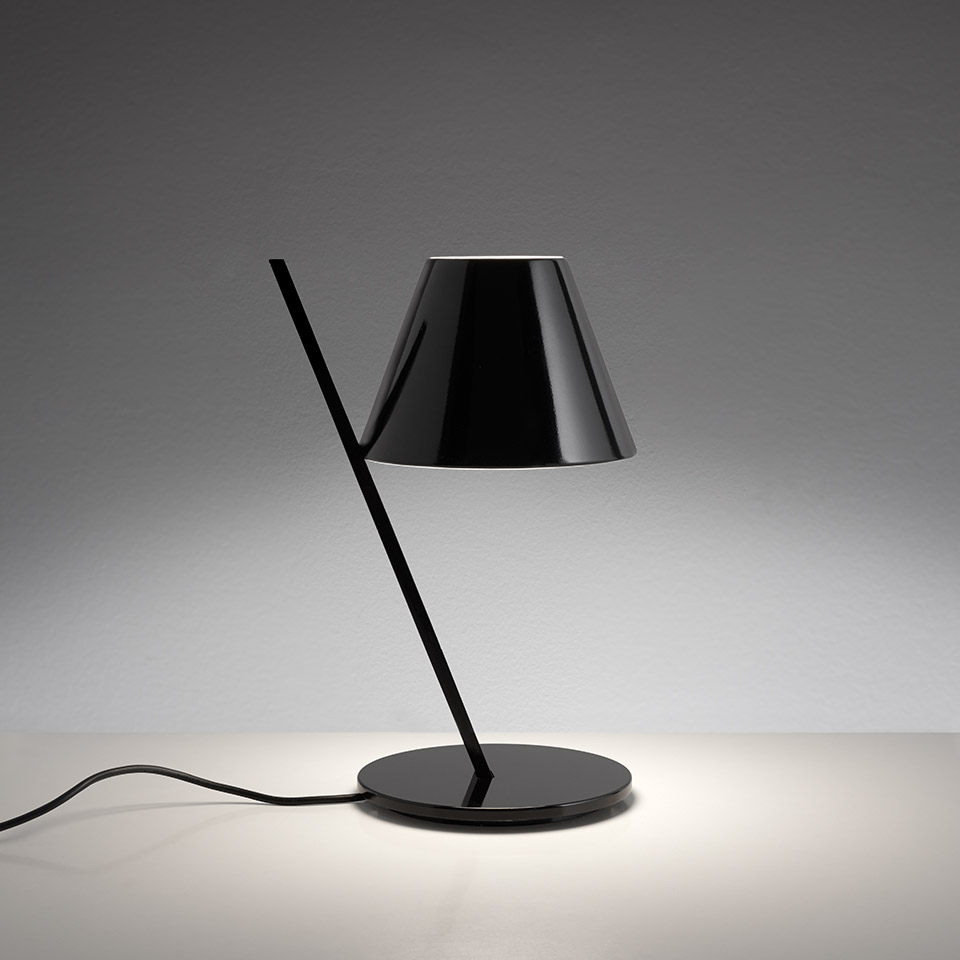 Lampada da tavolo Artemide La Petite nera: stelo diagonale su base rotonda, paralume conico lucido che dirige luce calda verso il basso