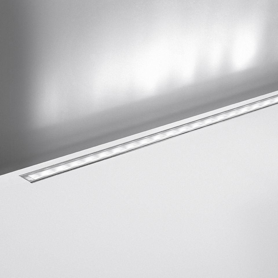 Artemide LineaLed Wallwasher: sottile apparecchio LED lineare incassato a filo nel soffitto bianco, con luce diffusa verso la parete